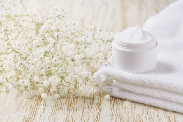 Crème anti-rides anti-âge soins du corps et soins du visage hygiène lotion hydratante avec des fleurs blanches dans un pot en plastique sur une table en bois.