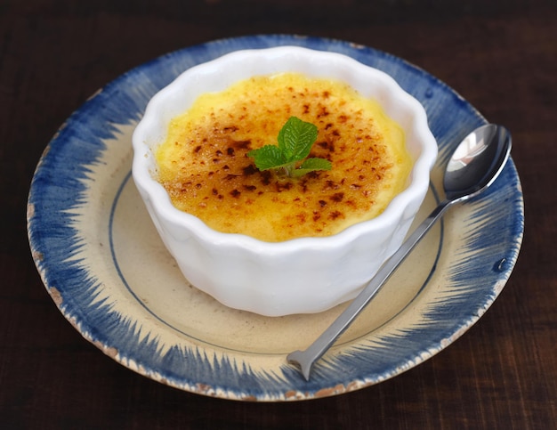 Crème brûlée dans un bol en céramique sur table en bois et fond noir