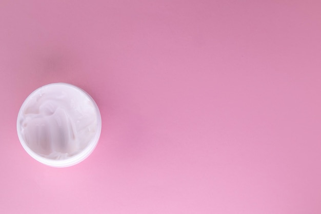 Crème cosmétique blanche pour le visage dans un pot rond ouvert sur fond rose vue de dessus copie de l'espace à droite