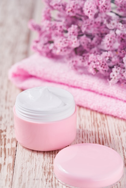 Crème cosmétique cicatrisante à base de plantes, produit de soin de la peau hygiénique ou masque de maquillage relaxant dans un pot rose avec une serviette sur une table en bois.