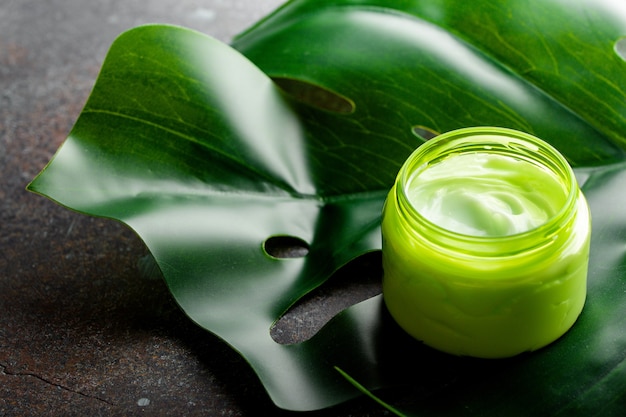 Crème cosmétique dans un récipient sur une vue d'angle de feuille tropicale de monstera verte, cosmétiques naturels et concept de produit de soin de la peau biologique. Crème pour les soins du visage et du corps, fond cosmétique avec espace de copie