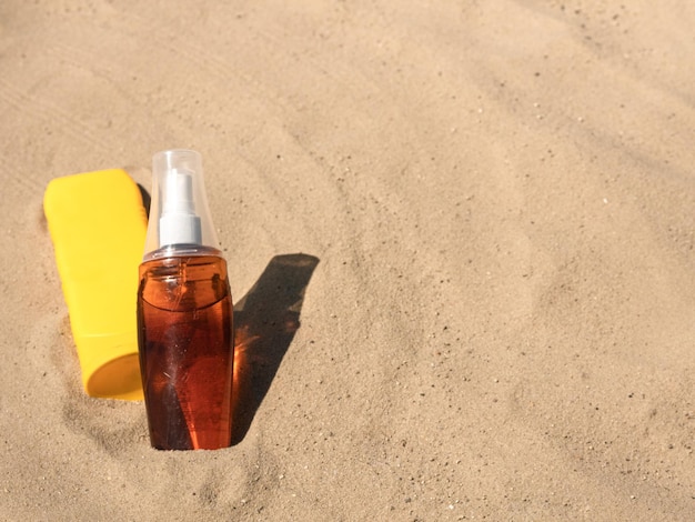 La crème cosmétique et l'huile de bronzage dans une bouteille jaune et transparente sur le sable est une place pour le texte