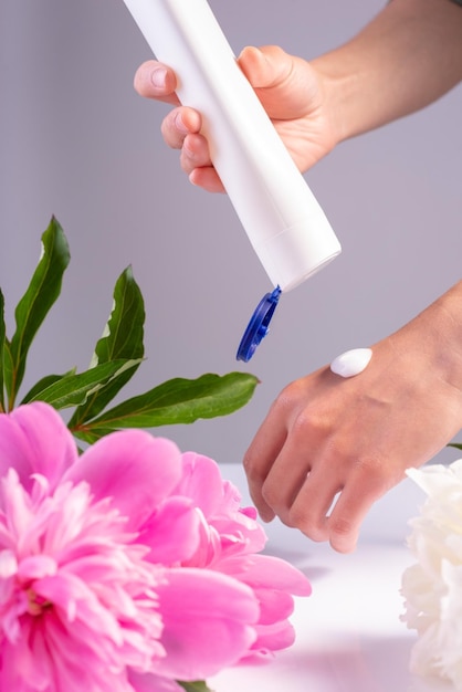 Crème cosmétique pour les mains féminines avec des fleurs sur fond blanc