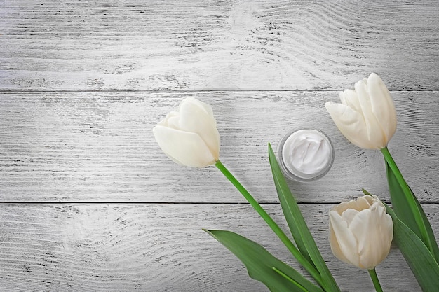 Crème cosmétique avec tulipes sur fond de bois blanc