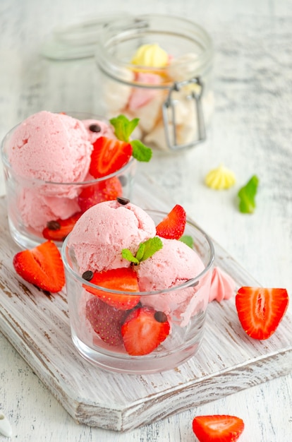 Crème glacée aux fraises dans un verre avec des fraises fraîches, des gouttes de chocolat et de la menthe sur une planche