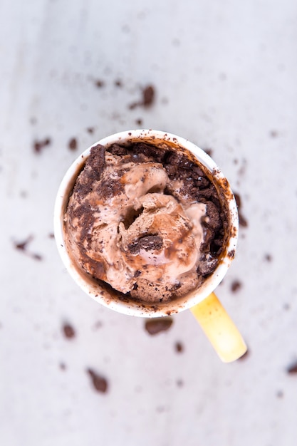 Photo crème glacée brun chocolat dans une tasse et une cuillère jaune ordinaire, vue de dessus, avec garniture et miettes.