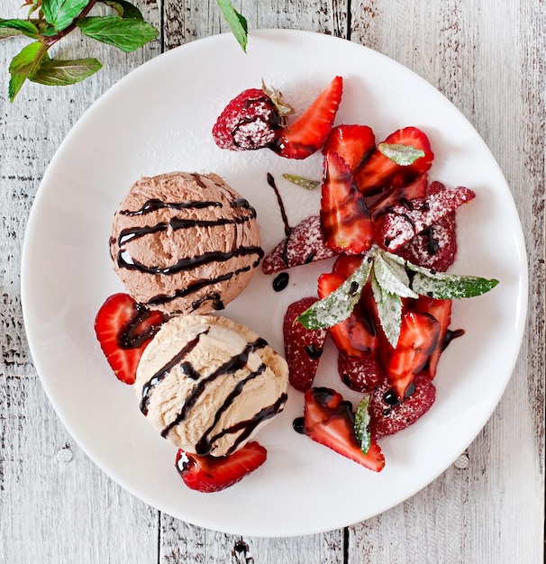 De la crème glacée avec des fraises et du chocolat sur une assiette blanche.