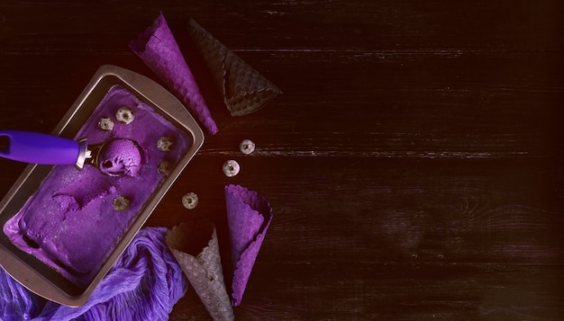 Crème glacée violette avec une spatule pour la crème glacée sur un fond en bois foncé avec des tasses à gaufre