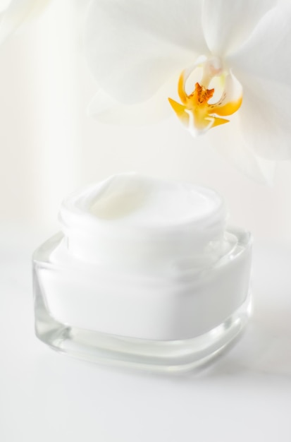 Crème hydratante pour le visage dans un pot et fleur d'orchidée en fleurs sur fond blanc cosmétiques de soins de la peau