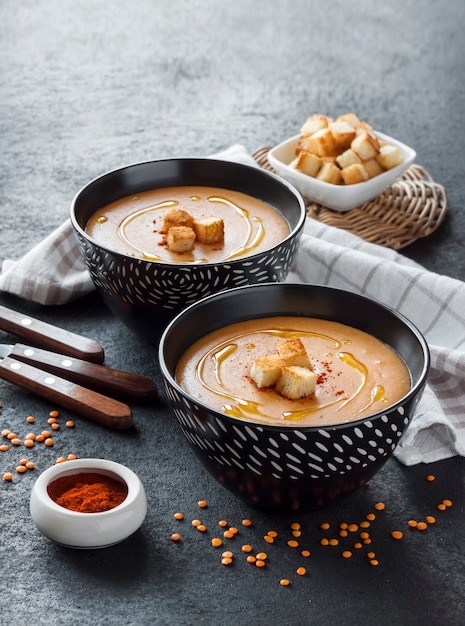 Photo crème de lentilles au paprika et croûtons dans des bols en céramique noire sur fond sombre. espace de copie