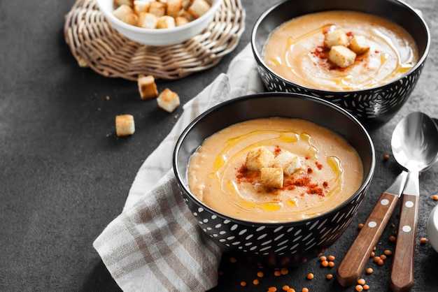 Crème de lentilles au paprika et croûtons dans des bols en céramique noire sur fond sombre. Espace de copie