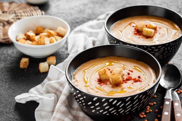 Crème de lentilles au paprika et croûtons dans des bols en céramique noire sur fond sombre