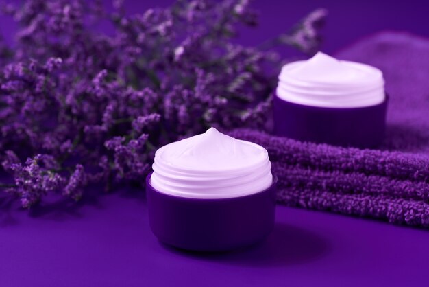 Crème ou lotion naturelle pour le visage de nuit, cosmétique biologique pour hydrater la peau avec une serviette et des fleurs en arrière-plan.