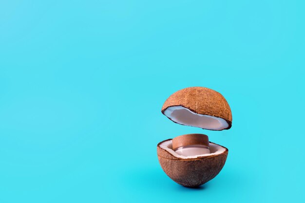 Crème de noix de coco dans un bocal en verre avec de la noix de coco fraîche divisée en deux et volant sur fond turquoise