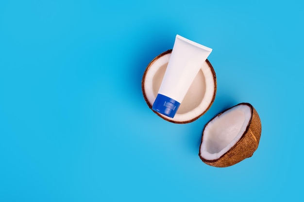 Crème de noix de coco dans un tube en plastique avec de la noix de coco fraîche divisée en deux sur fond bleu isolé