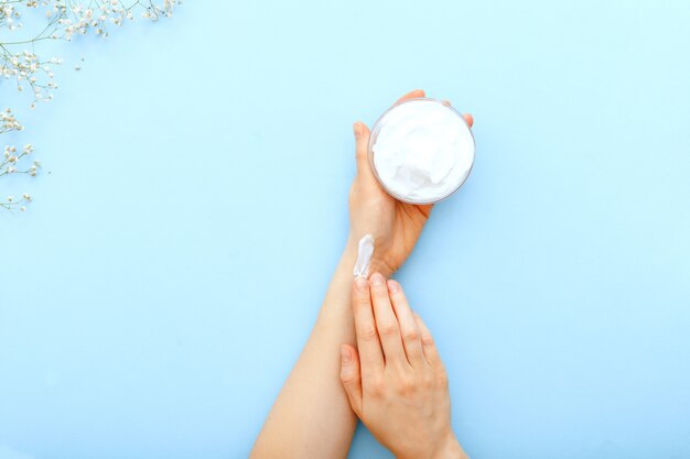 Photo crème pour les mains, mains féminines appliquant des cosmétiques crème naturelle bio sur bleu