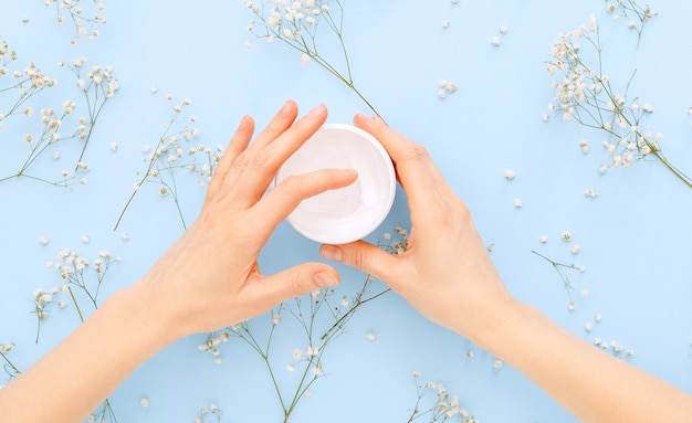 Crème pour les mains, mains féminines appliquant des cosmétiques à la crème naturelle biologique sur un fond de couleur bleu pastel. Crème de soin de la peau en pot pour les mains, le corps.