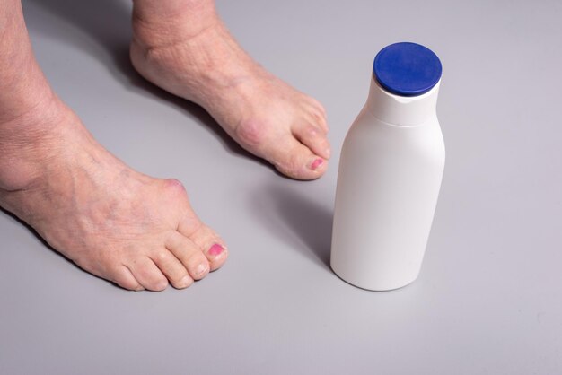 Crème pour les pieds vieille femme appliquant de la crème d'un tube aux pieds sur fond gris