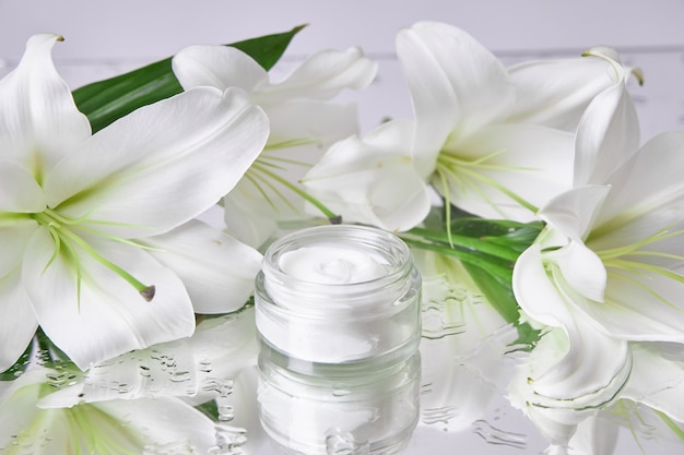 Crème pour les soins de la peau, cosmétiques naturels à base de fleurs et de pétales. Un pot en verre de crème blanche se dresse parmi les fleurs de lys