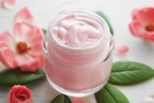 Crème pour le visage et fleurs roses sur fond de bois blanc