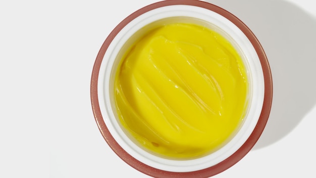Crème pour le visage jaune dans un pot sur fond blanc cosmétiques hydratants
