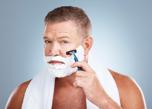 Photo crème à raser visage et homme avec rasoir en studio isolé sur fond bleu pour l'épilation portrait soins de la peau et modèle masculin mature avec mousse faciale à raser pour l'esthétique santé ou bien-être