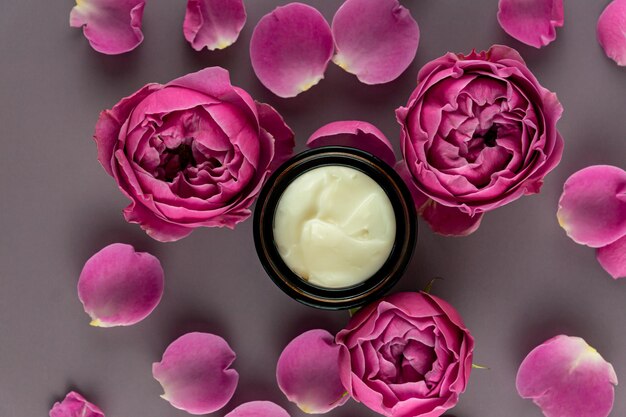 Crème de soin du visage dans un pot sur fond marron avec de belles roses. crème anti-âge. Crème pour les soins de la peau. Concept de soins de beauté.