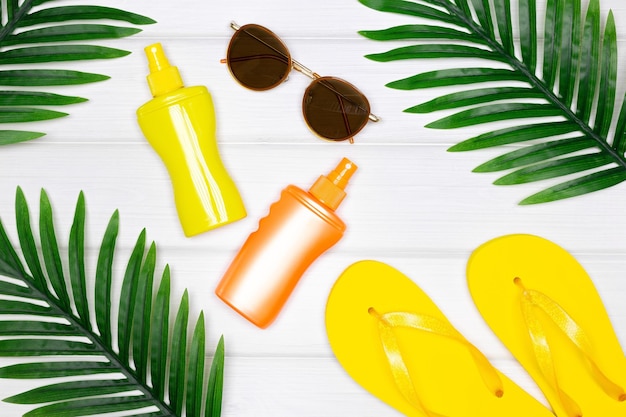 Crème solaire produits de bronzage lunettes de soleil tongs sandales avec feuilles de palmier tropicales Ambiance estivale