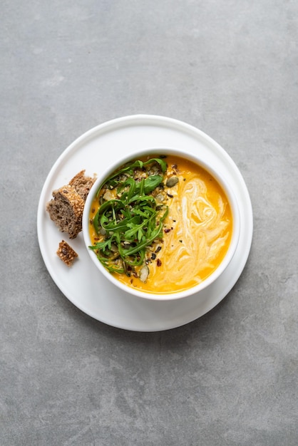 Crème de soupe aux carottes dans un bol blanc Bol de soupe aux carottes avec des feuilles de roquette sur une table en béton