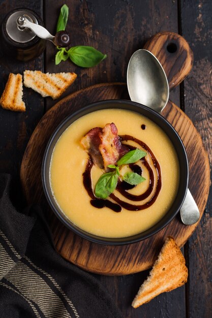 Crème de soupe de pommes de terre au bacon et sauce soja dans un bol noir, sur une surface de béton ancienne sombre