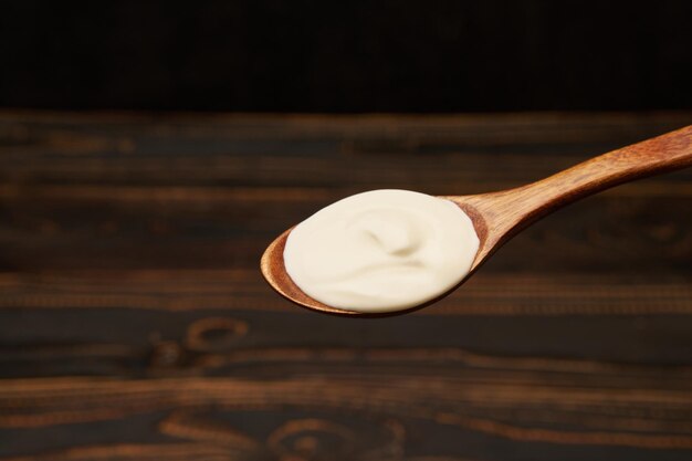 Crème sure dans une cuillère en bois sur fond de bois