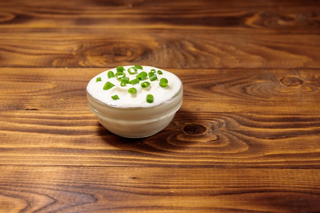 Crème sure à l'oignon vert dans un bol en verre sur une table en bois