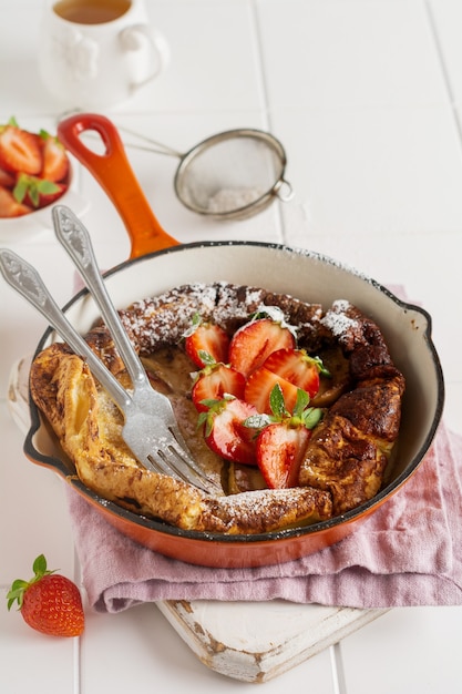 Crêpe de bébé hollandais avec baies de fraises fraîches et saupoudrées de sucre glace en poudre dans une poêle rouge sur fond de cuisine blanche Vue de dessus.