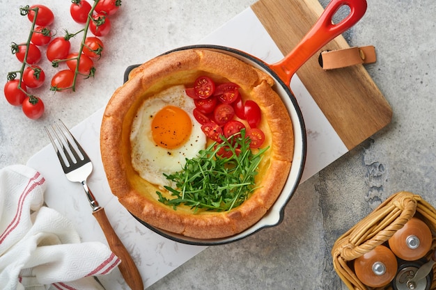 Crêpe hollandaise pour bébé Crêpe hollandaise fraîche faite maison pour bébé avec œuf frit tomate et roquette verte dans une poêle en fonte de roseau sur une table rustique en béton gris clair Mise à plat en gros plan