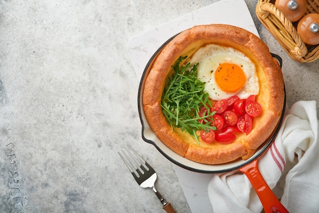 Crêpe hollandaise pour bébé Crêpe hollandaise fraîche faite maison pour bébé avec œuf frit tomate et roquette verte dans une poêle en fonte de roseau sur une table rustique en béton gris clair Mise à plat en gros plan