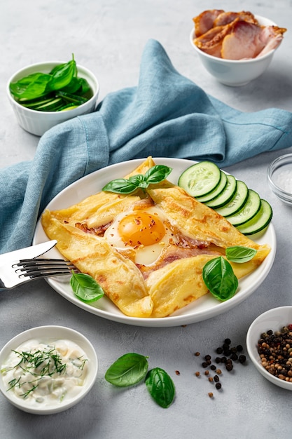 Crêpe avec oeuf, jambon et fromage saupoudré de basilic sur un mur gris. Vue latérale, verticale.