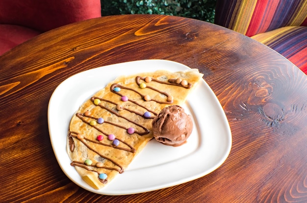 Crêpe sucrée avec crème au chocolat et crème glacée sur fond de bois