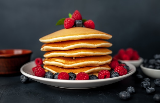 Crêpes américaines aux framboises, bleuets frais et miel. Petit déjeuner sain sur béton