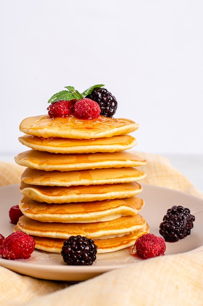 Crêpes américaines classiques faites maison avec des framboises fraîches, des mûres, du miel et des feuilles de menthe, sur une surface claire