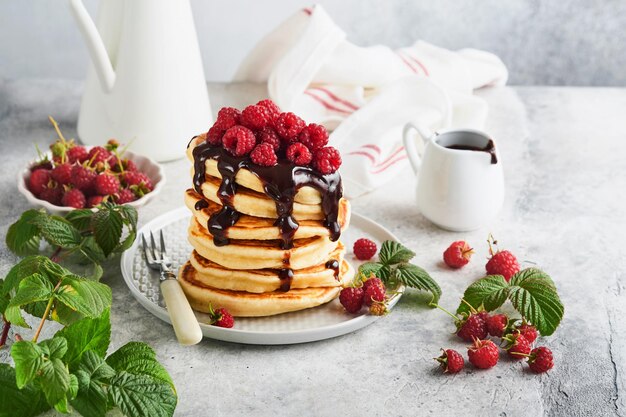 Crêpes américaines Empilez des crêpes avec des framboises fraîches avec du glaçage au chocolat ou des garnitures dans un bol blanc sur fond de table gris clair Crêpes américaines classiques faites maison Concept de magazine Vue de dessus