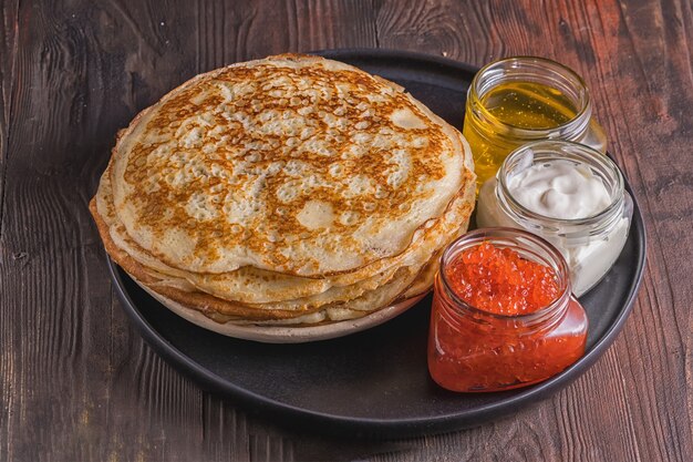 Crêpes sur une assiette avec caviar rouge, miel et crème.