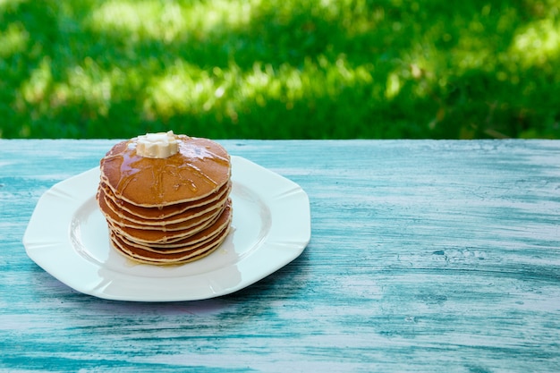 Crêpes au beurre et au miel sur une plaque blanche dans un jardin en bois bleu ou dans la nature. Pile de crêpes dorées au blé ou gâteau aux crêpes, gros plan.