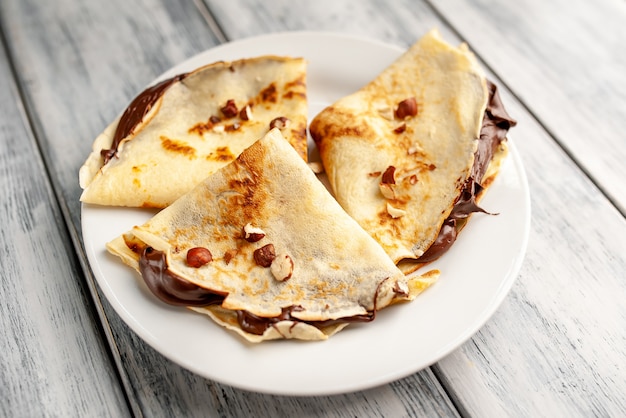 Crêpes au chocolat et aux noisettes, sur une plaque blanche sur un fond de bois