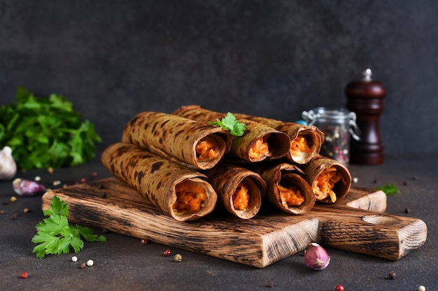 Crêpes au foie et farce aux carottes sur une planche de bois sur fond sombre.