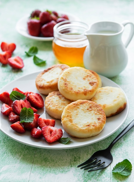 Crêpes au fromage cottage, beignets de ricotta sur plaque en céramique avec fraise fraîche. Petit déjeuner sain et délicieux le matin.