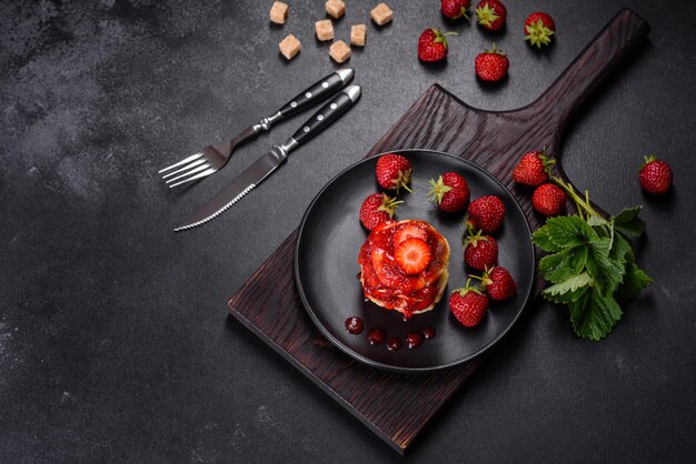 Crêpes au fromage cottage avec fraises tranchées et confiture de fraises sur une assiette sur fond de béton