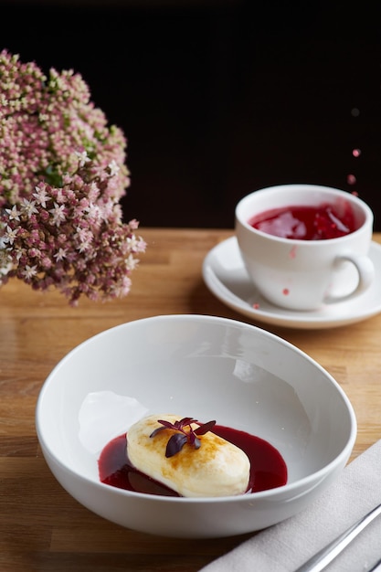 Crêpes au fromage cottage avec sauce aux baies et thé rouge. table du matin du petit déjeuner avec des fleurs.