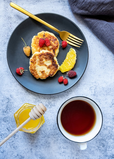 Crêpes au fromage cottage ou syrniki russe avec des baies et du miel et une tasse de thé servi pour le petit déjeuner