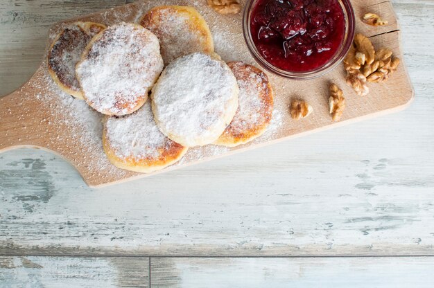 Photo crêpes au fromage fait maison avec du sucre en poudre avec de la confiture de framboise et des noix se trouvent sur une planche de bois