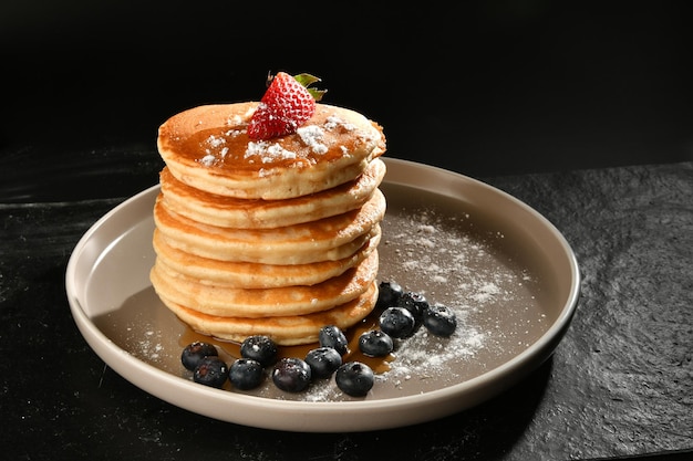 crêpes au sucre, fraises et myrtilles sur une texture sombre.